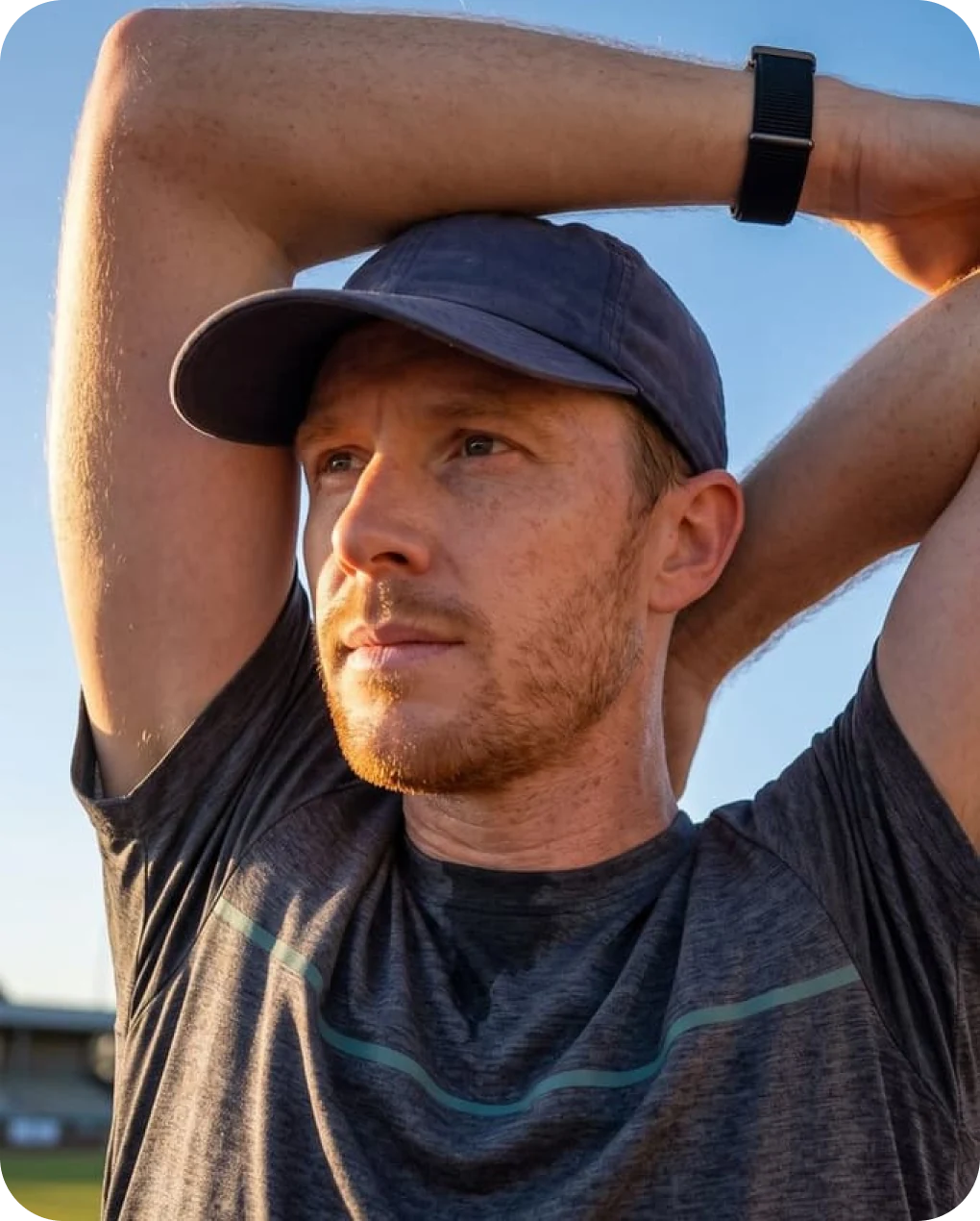 Man in a cap stretching his arms overhead at a running track, wearing the HLTH Band